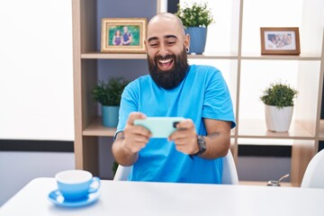 Young bald man playing video game by smartphone at home