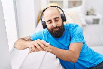 Young bald man listening to music sitting on sofa at home