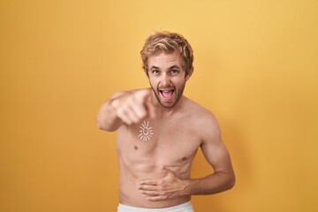 Fototapeta premium Caucasian man standing shirtless wearing sun screen laughing at you, pointing finger to the camera with hand over body, shame expression