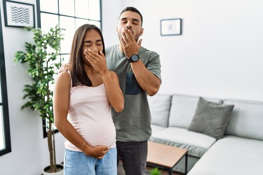 Young Interracial Couple Expecting A Baby, Touching Pregnant Belly Bored Yawning Tired Covering Mouth With Hand. Restless And Sleepiness.