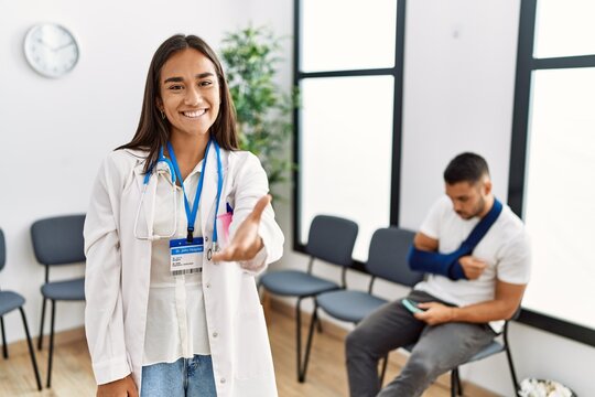 Young asian doctor woman at waiting room with a man with a broken arm smiling friendly offering handshake as greeting and welcoming. successful business.
