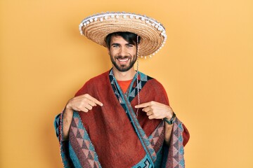 Young hispanic man holding mexican hat looking confident with smile on face, pointing oneself with...
