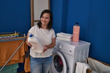 Down syndrome woman smiling confident holding detergent bottle at laundry room