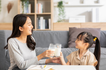 Asian mother and her daughter clink glasses enjoy and smile with milk drink.Mom and little girl...