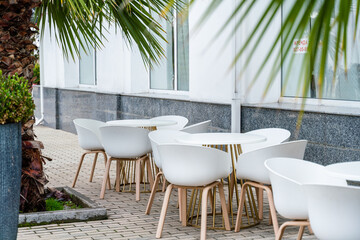 Street cafe with white chairs, green foliage around. Without people, tourism, travel.