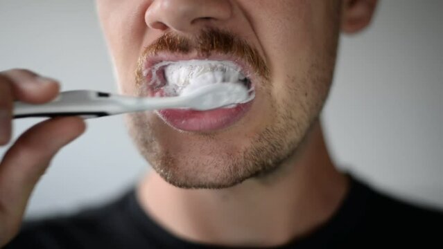 Close up footage of young man brushing teeth with grey tooth brush
