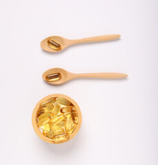 fish oil capsules, wood spoon and wood cup on white background and supplements concept