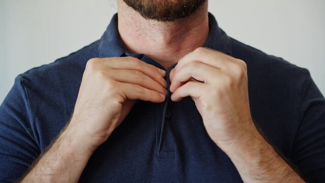 Hands buttoning a polo shirt not completely. Close-up of how to button the collar of a colored polo. Man adjusting his poloshirt collar undoing top button. Feeling relaxed and formal outfit.