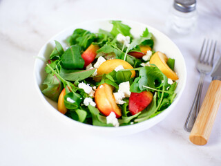 A light summer salad of rucolla, peaches and cheese on a light background.