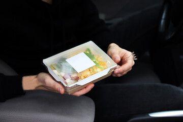 Man unpacking takeaway box with food in the car. Healthy food delivery service and daily ration...