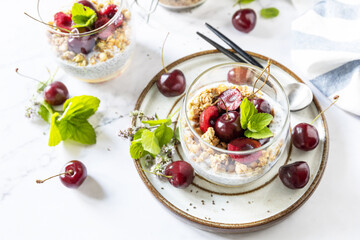 Healthy menu concept. Home made granola breakfast. Glass of parfait made of granola, berries cherry, yogurt with chia seeds on rustic table.