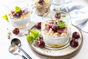 Healthy menu concept. Home made granola breakfast. Glass of parfait made of granola, berries cherry, yogurt with chia seeds on rustic table.