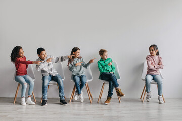 Naklejka premium Preteen Kids Laughing Pointing At Victimized Asian Schoolgirl Sitting Indoors
