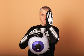 a 50-year-old man with gray hair holds a huge eye in his hand with his second hand covering his eye for Halloween 2022