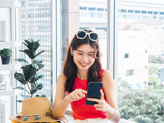 Young beautiful smiling Asian woman holding and using smart mobile phone, looking at screen. Happy...