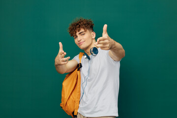 a close horizontal portrait of a handsome man with curly hair standing on a green background holding headphones around his neck and holding out his hands to the camera