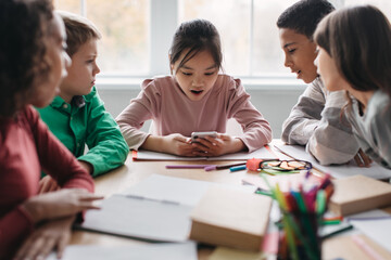 Classmates Using Smartphone Sitting At Desk During Break In Classroom