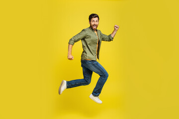 Fototapeta na wymiar Portrait of middle aged man running over yellow background, side view shot of joyful male jumping in air