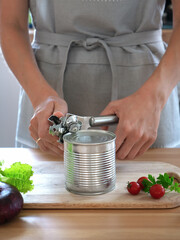 woman opens a can of canned food with a can opener in the kitchen