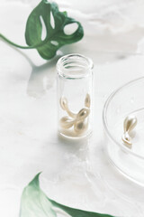 Various serum capsules for healthy skin routine. Anti-wrinkle rejuvenation skin treatment. Beauty product presentation. Off white stone marble background with monstera leaf.