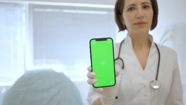 beautiful cute doctor in medical mask in medical office holds smartphone with chroma key in her hand. general practitioner. Doctor female dermatologist cosmetologist. 
