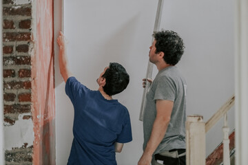 Two Caucasian male plasterer man checks the evenness of the walls after puttying.