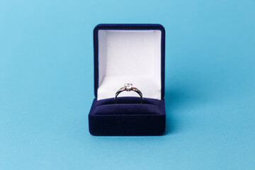 Jewelry, gold diamond ring in a blue box on a turquoise background, isolated.  A ring for a marriage proposal. Close-up. Front view. A place for your text.