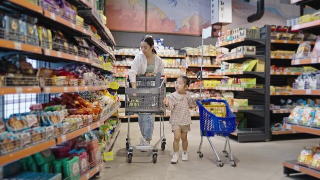 Preschooler girl helps mum to choose products in supermarket