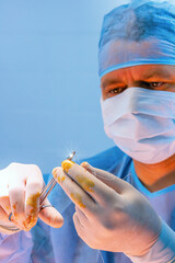 A professional surgeon holds a forceps with a needle and a suture thread - 524867954