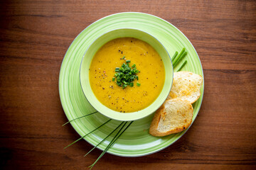 zupa krem z kabaczka i marchewki ze szczypiorkiem i grzankami na brązowym blacie - 524870396