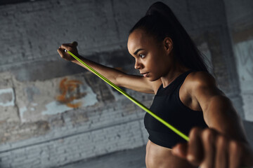 Concentrated young African woman using rope while doing stretching exercises in gym - Powered by Adobe