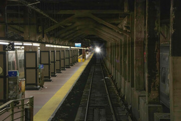 Obraz premium View looking down tracks in an underground train platform with train lights approaching, nobody