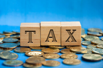 Tax word engraved on wooden block surrounded with gold coins. Taxation concept