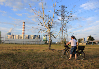 Mężczyzna z rowerem turystycznym przed uschniętym drzewem brzozy, elektrownia. - obrazy, fototapety, plakaty