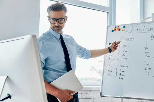 Male English teacher pointing whiteboard while having web conference at the classroom