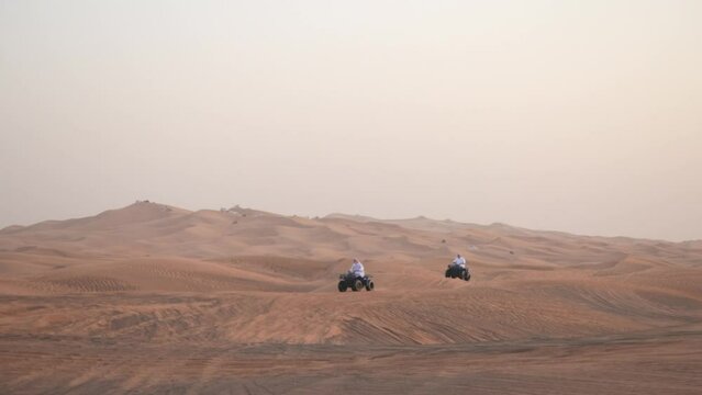 people in white kundurs on quad bikes on a safari in the UAE desert ride on dunes