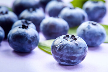 Close-up of a blueberry with green leaves and water drops on a purple background