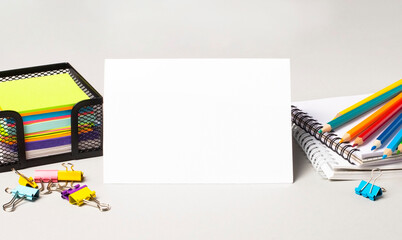 Paper card with space to insert text, multi-colored pencils, stickers and paper clips on the desktop. Copy space