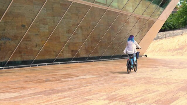 View from behind of the Woman Riding On Rent electric bicycle. Urban Style Green Energy City Transport. Ecological Transportation Mobility In City.