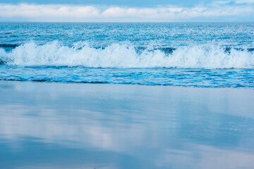 Naklejka na ściany i meble seascape, ocean surf on a smooth sandy beach, the sky is reflected in the wet sand