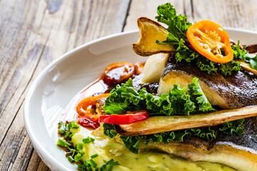 Fish dish - fried halibut with potato puree, fried pepper and chorizo on wooden table
