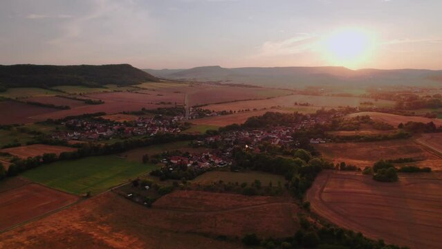 Aer ial view of a German village surrounded by meadows, farmland and forest at sunset in Germany.