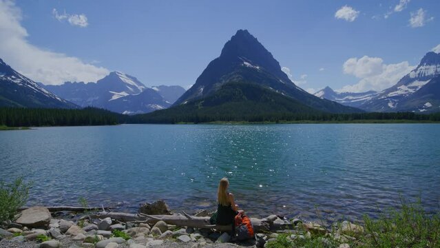 Lush vegetation on shoreline of beautiful mountainous landscape with glacier peaks in the background. Solo female traveler enjoying tranquil, rustic natural environment. High quality 4k footage