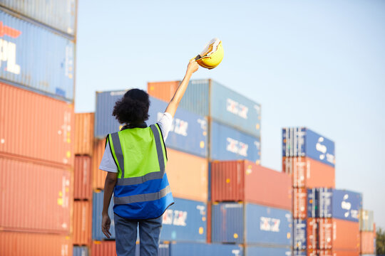 back view factory worker or engineer raising hands up and holding helmet in containers warehouse storage