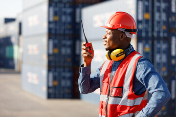 African factory worker or engineer using walkie talkie and talking about work in containers...