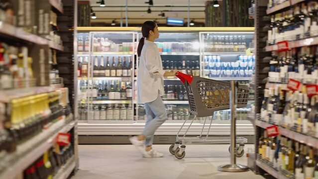 Asian woman does shopping with trolley for goods in store