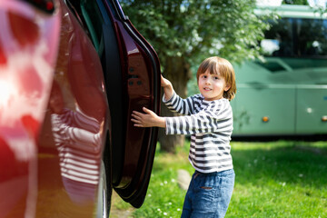 Preschool boy opening a door of family car on the parking, child ready to sit into an auto, safe travelling with kids