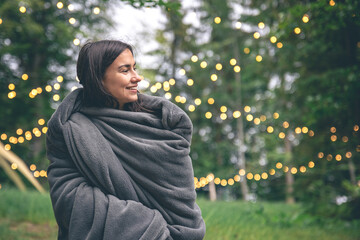 A young woman wrapped in a blanket in the forest on a blurred background.