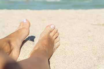 Close-up of the feet of an unrecognizable woman in the foreground with her nails pitted in the beach sand with the sea in the background.
