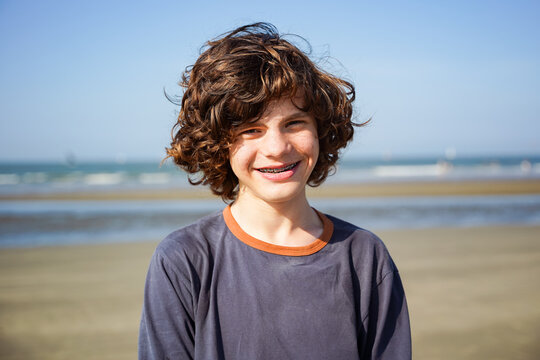 Close up portrait of a teenager boy with curly hair, acne and dental braces. Positive child of forteen years old, outdoor, at the sea.